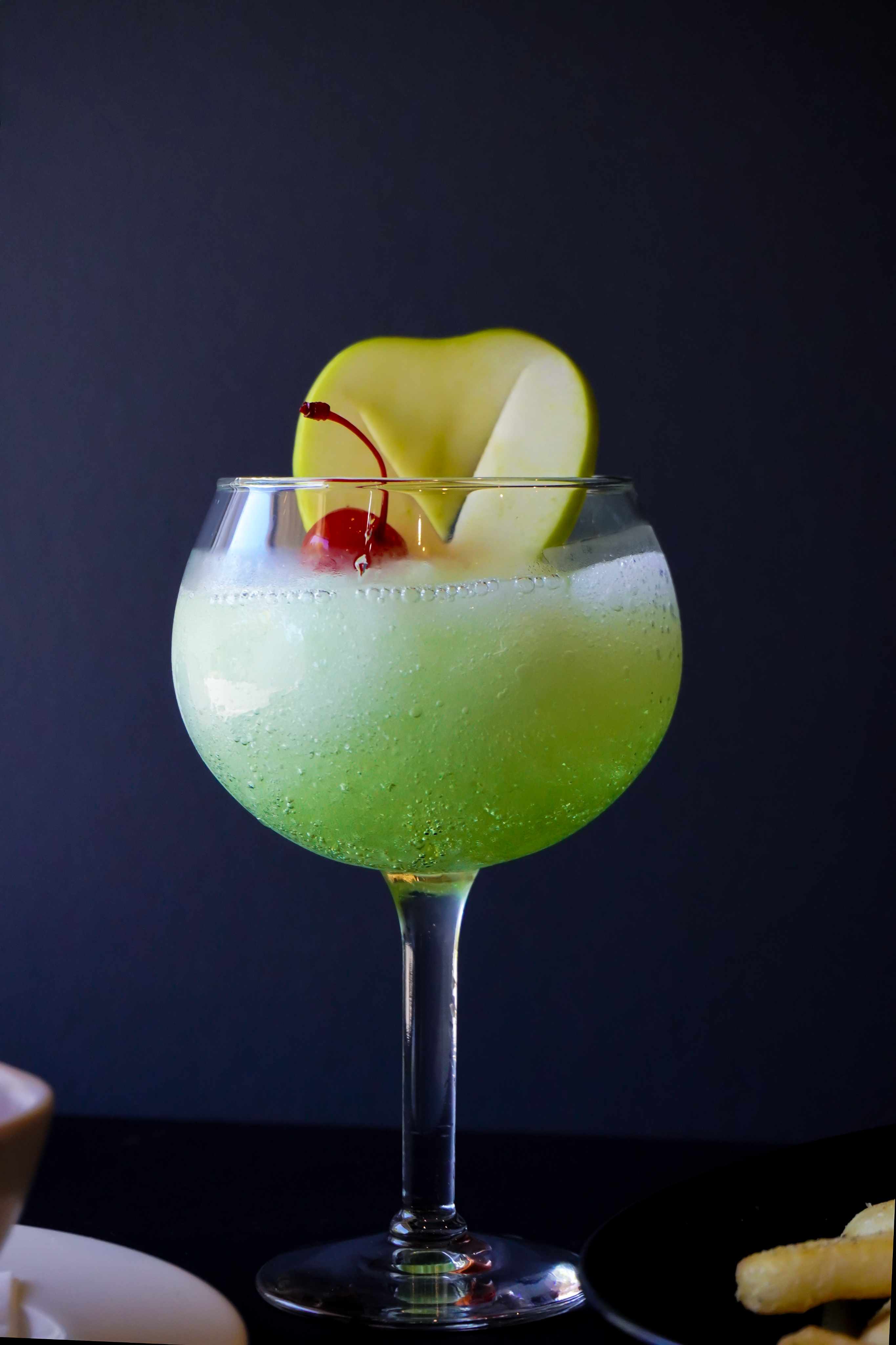PLACEHOLDER — Cocktail - 1.png: bright green frozen cocktail with apple fan and cherry garnish